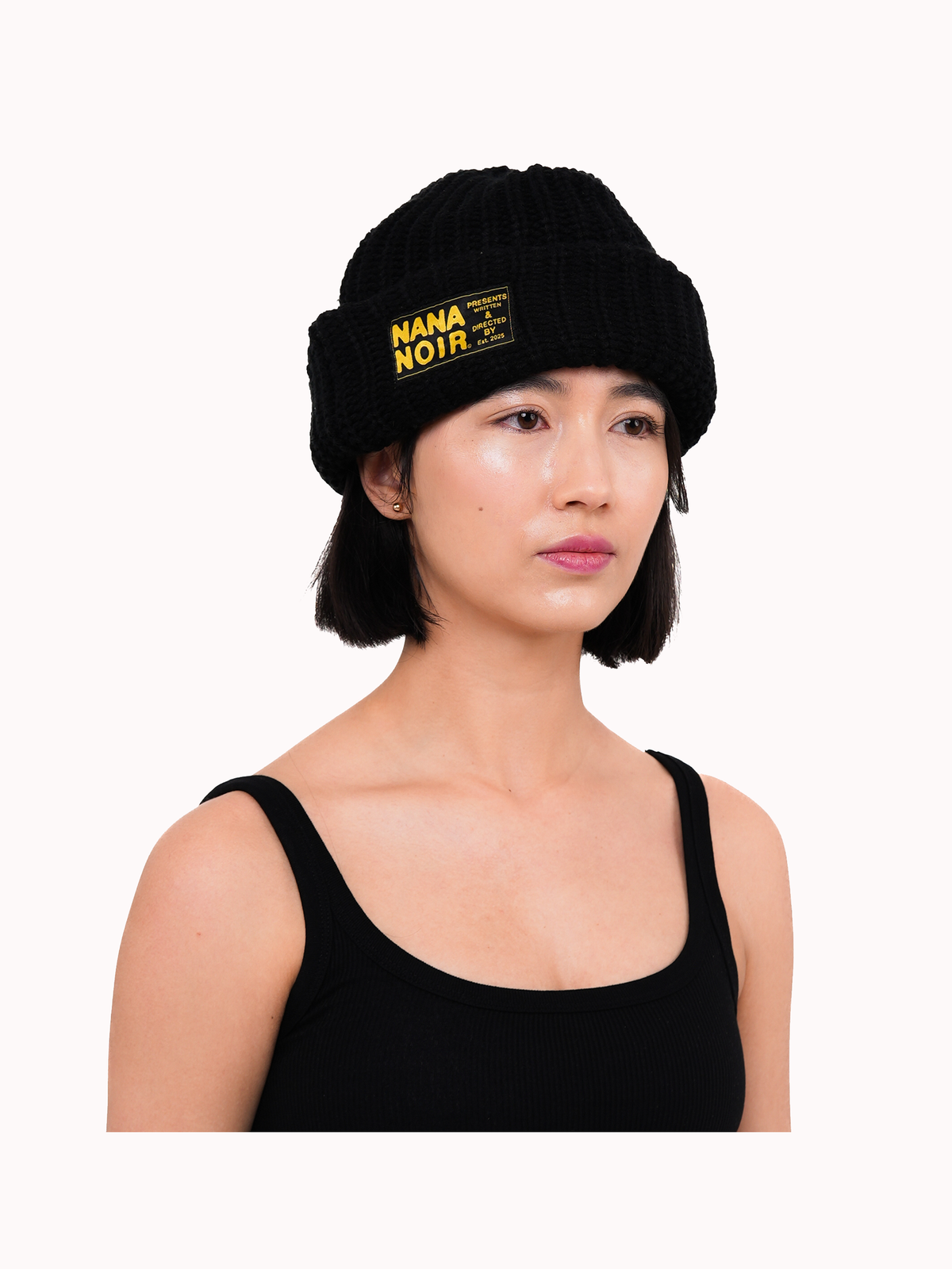 Model wearing the CHECK IN black crochet beanie with oversized cuff and yellow Nana Noir patch