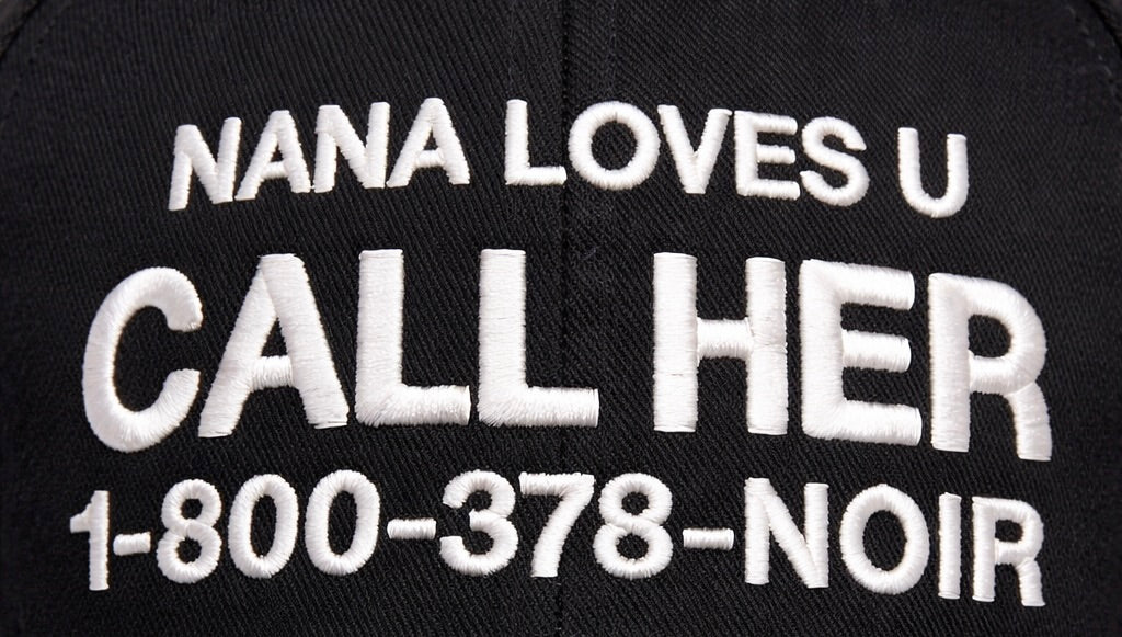 Close-up of white CALL HER slogan embroidery on black cotton cap